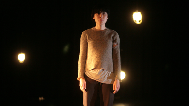 Aretha Aoki in a rehearsal of <i>Niicugni (Listen)</i>, fish skin lanterns light the background.